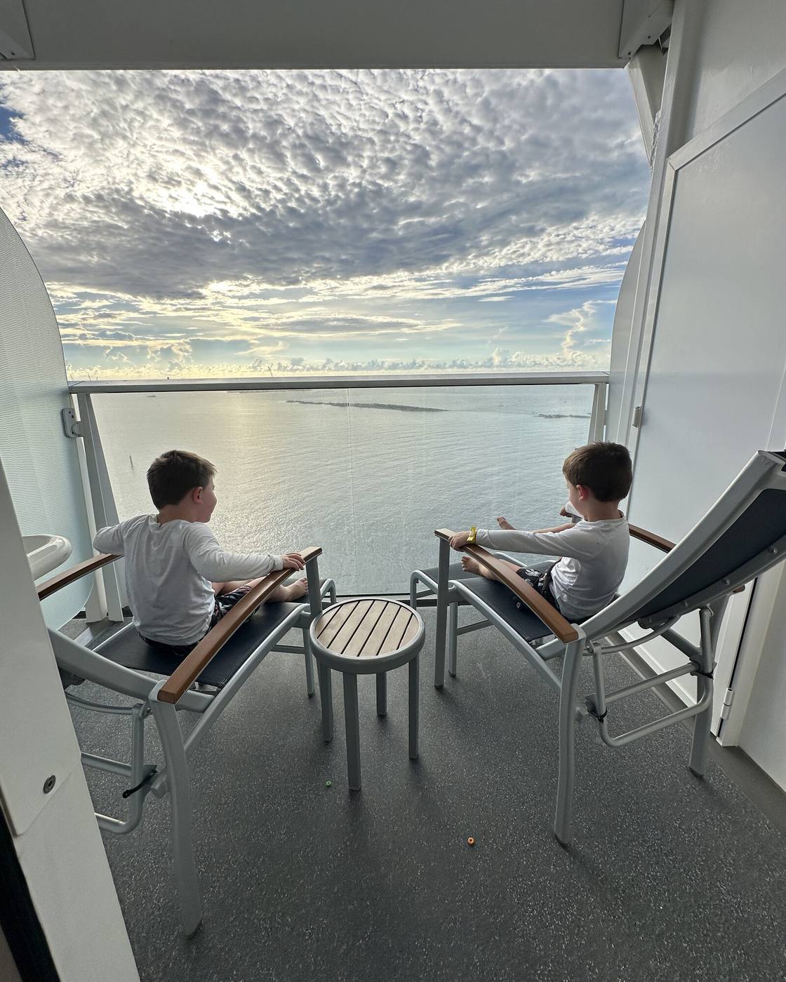 Two children on a cruise ship balcony watching the sunrise over a calm sea