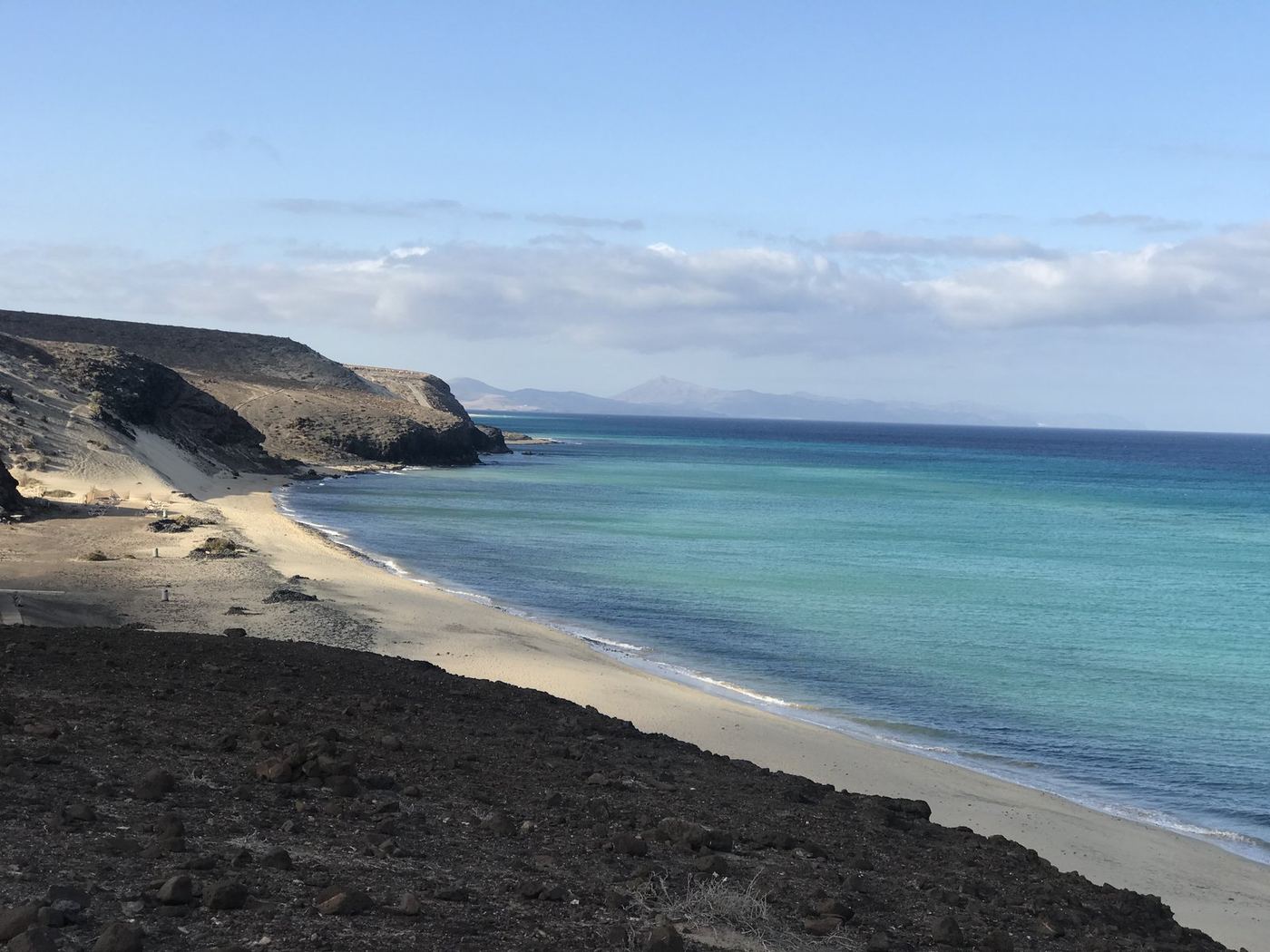 A quiet turquoise cove with golden sand and a rugged volcanic coastline