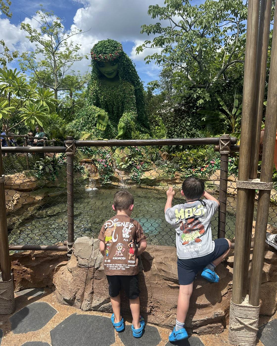 Two children taking in a Disney garden sculpture across the water