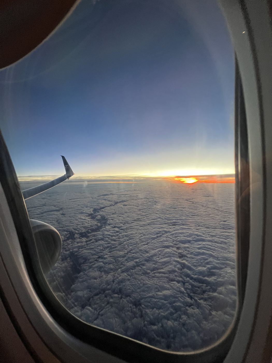 Sunset over the clouds from an airplane window, the wing catching the last light